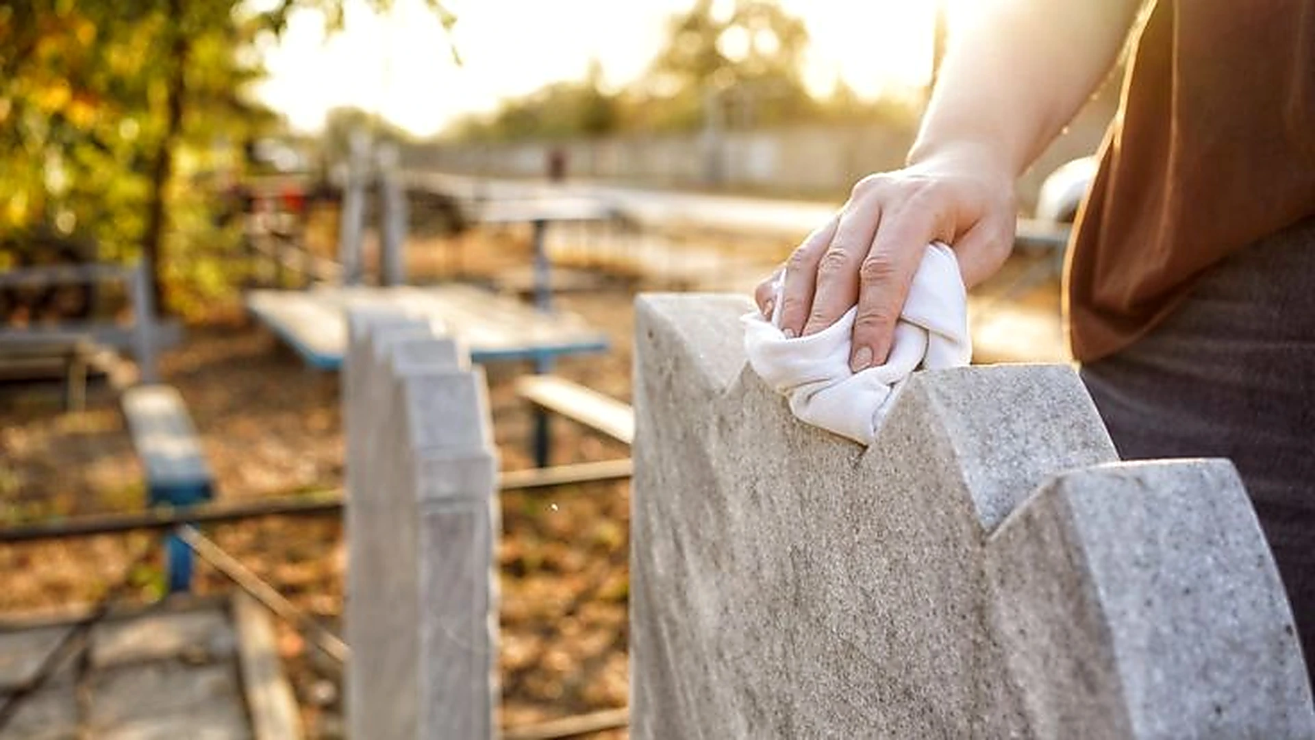 Hand-wiping a light stone headstone with a soft cloth in warm sunlight